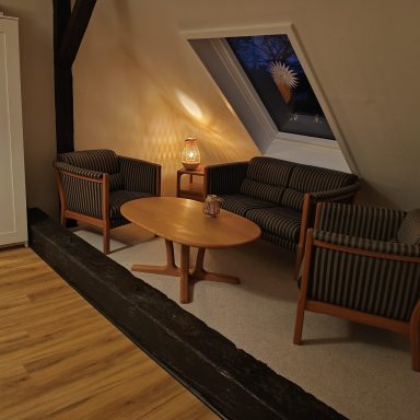 Livingroom 2 Gemütliche Sitzecke mit zwei Sofas und einem Tisch unter einem schrägen Fenster.