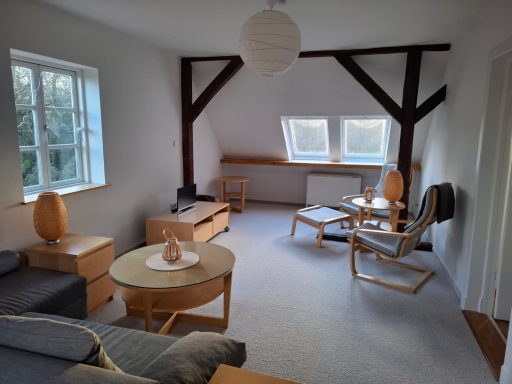 Livingroom 1 Heller Wohnraum mit Holzdetails, Sofa, Sesseln und einem runden Tisch.