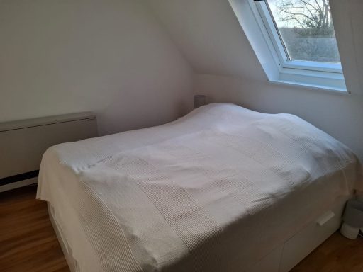 Stralight room Helles Schlafzimmer mit einem Bett und schrägen Wänden unter einem Fenster.